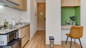 A compact kitchen with a microwave, stove, and sink, a wooden cabinet, and a green wall with a desk and chair. - w Amazing Loft in the Heart of Chico Norte (Bogotá)