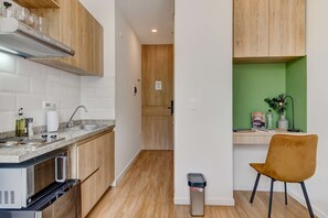A compact kitchen with a microwave, stove, and sink, a wooden cabinet, and a green wall with a desk and chair. - w Amazing Loft in the Heart of Chico Norte (Bogotá)