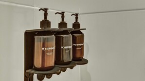 A bathroom with a wall-mounted shelf holding three bottles of Wynywood liquid soap. - w Amazing Loft in the Heart of Chico Norte (Bogotá)