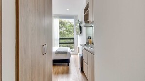 A modern bedroom with a bed, a view of greenery outside, and a kitchen area with cabinets and a sink. - w Amazing Loft in the Heart of Chico Norte (Bogotá)