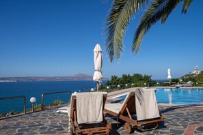A poolside area with lounge chairs and an umbrella, overlooking a body of water and a distant mountain. - Crete Thea Beachfront Escape With Pool Seaviews (Apokoronas)