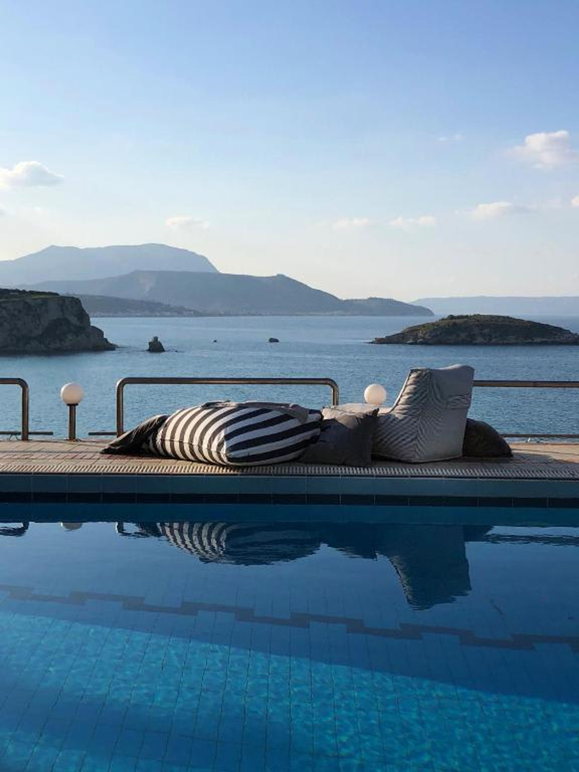 A poolside area with a view of the sea and distant mountains.