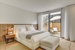 Ein modernes Schlafzimmer mit einem großen Bett, einem Nachttisch mit Lampe und Blick auf eine Terrassenanlage.