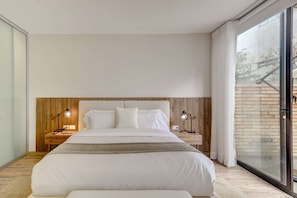 Ein modernes Schlafzimmer mit einem großen Bett, einem Holz-Kopfteil, Nachttischlampen und Blick durch eine Glastür.