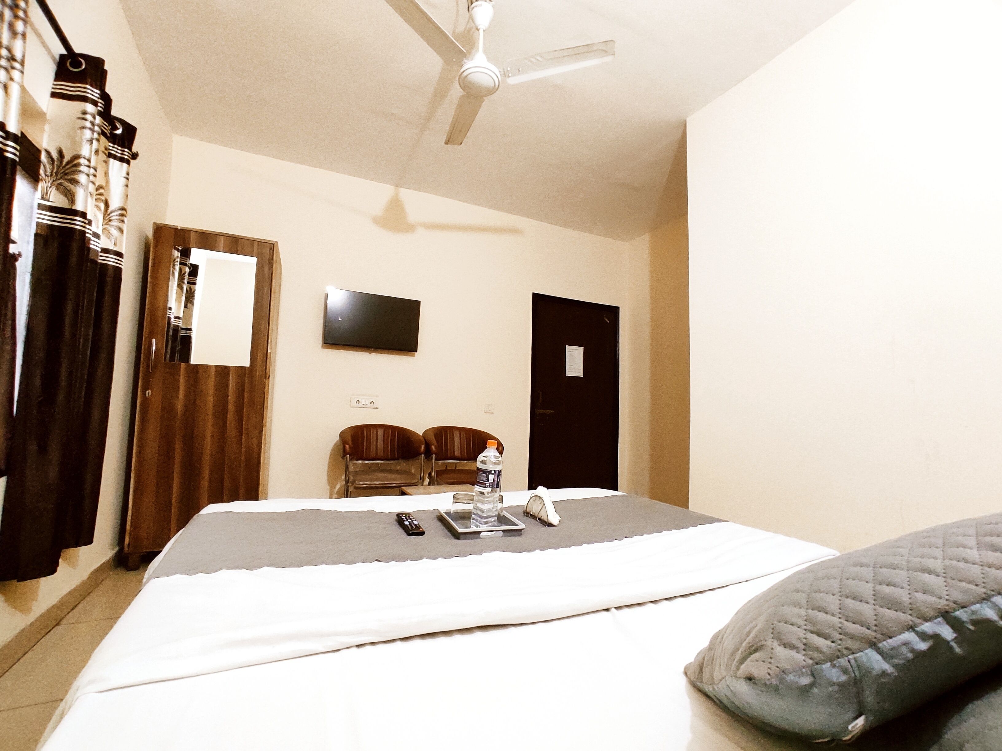 A hotel room with a bed, a ceiling fan, a TV, and a door.