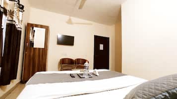 A hotel room with a bed, a ceiling fan, a TV, and a door.