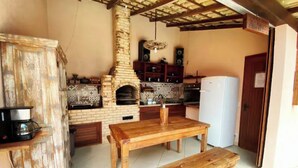 A rustic kitchen with a brick oven, wooden table, and bench. - Flamboyant Space - Armação dos Búzios - Near the Beach (Armação dos Búzios)