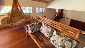 A wooden ceiling, a hanging chair, a wooden bench with floral cushions, and a view of a pool through a window. - Flamboyant Space - Armação dos Búzios - Near the Beach (Armação dos Búzios)