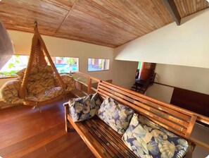 A wooden ceiling, a hanging chair, a wooden bench with floral cushions, and a view of a pool through a window. - Flamboyant Space - Armação dos Búzios - Near the Beach (Armação dos Búzios)
