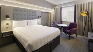 A hotel room with a large bed, a small round table, a purple chair, and a floor lamp. - Premier Inn Braintree (Braintree)