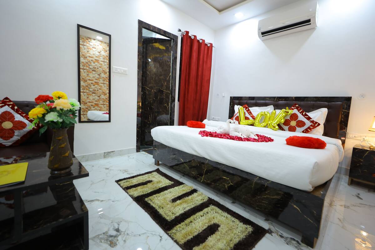 Un dormitorio moderno con una cama, una mesita de noche, un jarrón con flores, un espejo y una cortina roja.