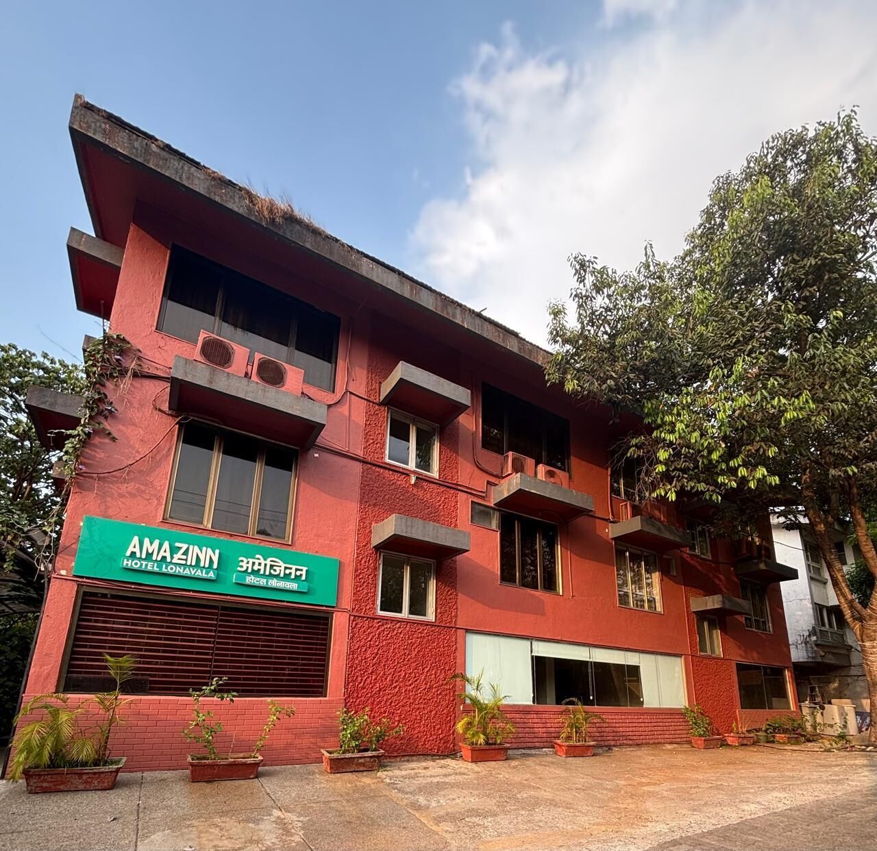A red building with a sign for 'AMAZINN HOTEL LONAVALA' and balconies.