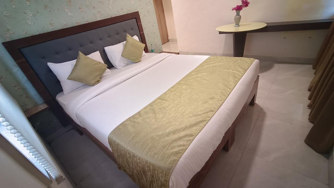 A neatly made bed with a headboard, a bedside table with a vase of flowers, and a curtain on the right.