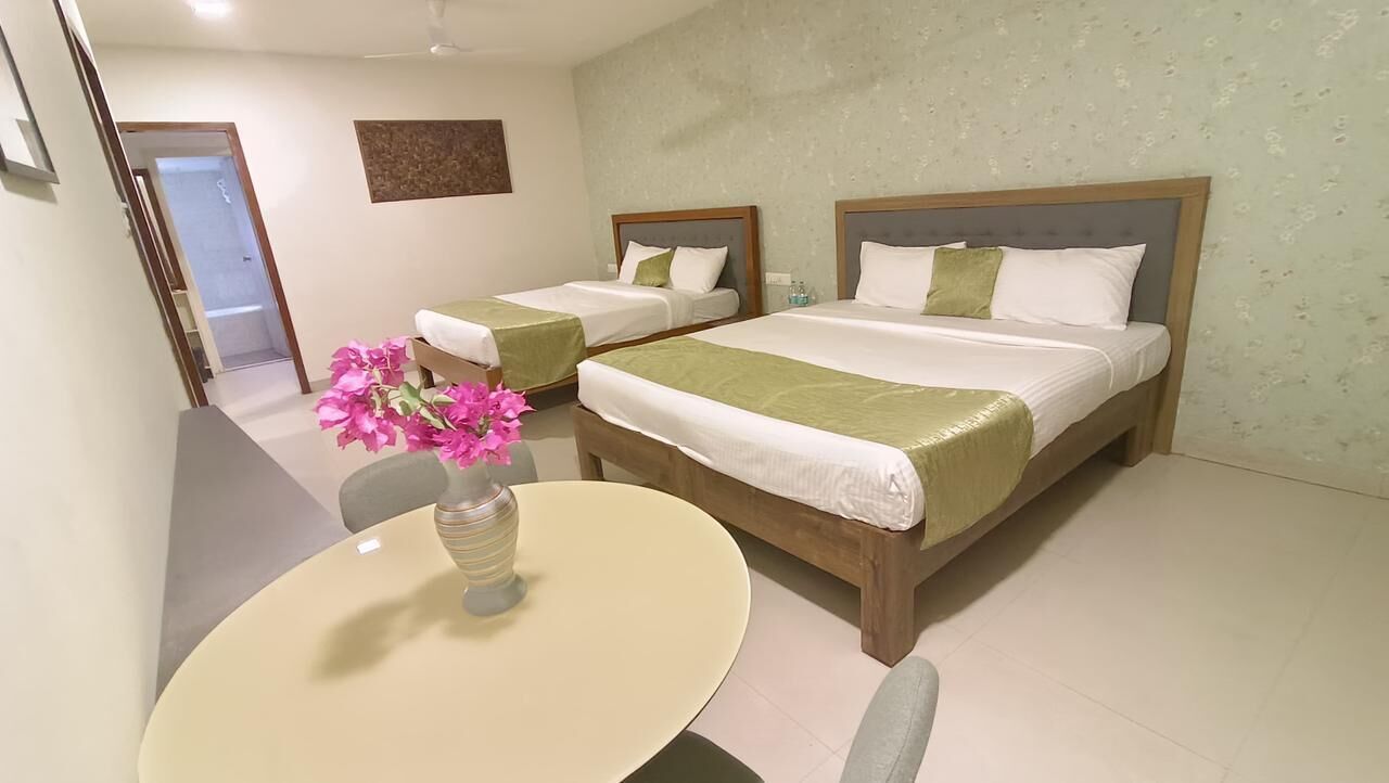 A hotel room with two beds, a dining table, and a vase of flowers.