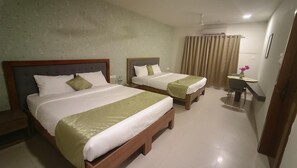 A hotel room with two beds, a desk, and a bathroom with curtains. - Amazinn Hotel (Lonavala)