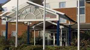 Un hotel con entrada cubierta, varias banderas y fachada de ladrillo.