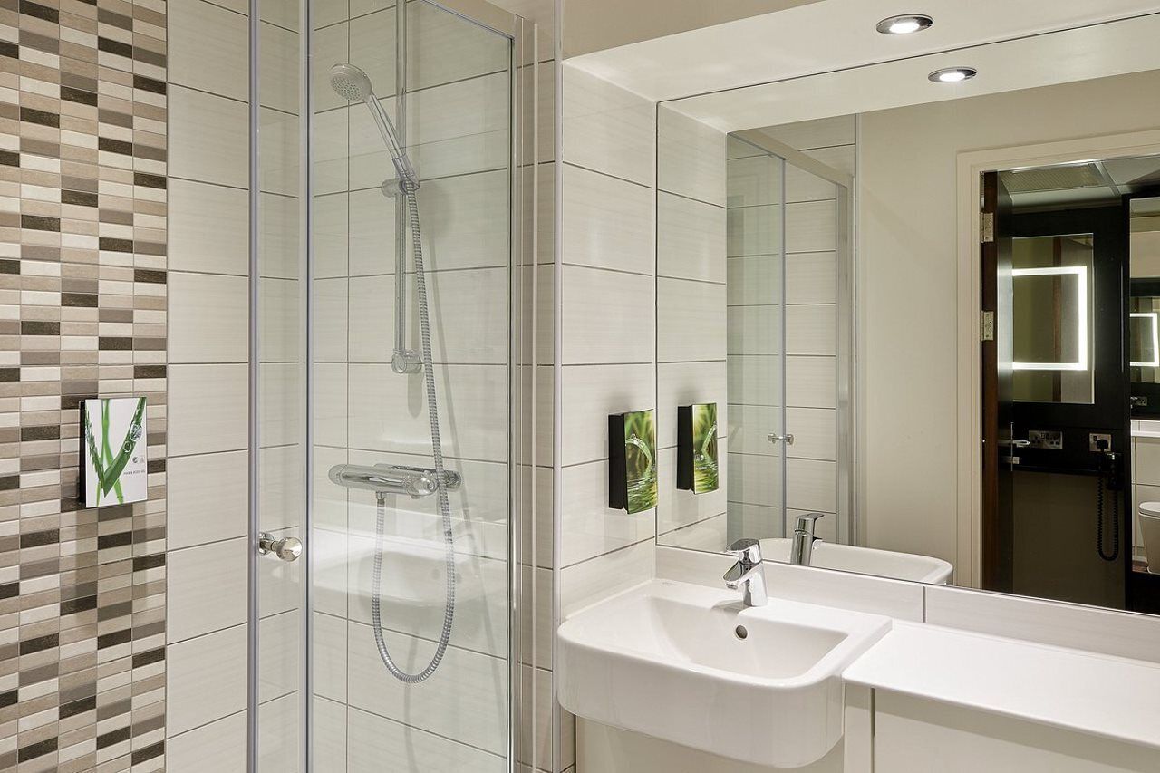 A modern bathroom with a glass-enclosed shower, a white sink, and a large mirror.