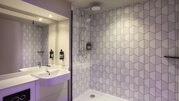 Un baño moderno con cabina de ducha de vidrio, dos lavamanos y un espejo grande.