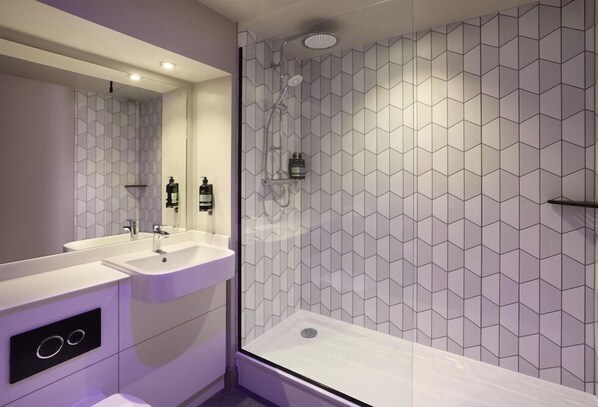 Un baño moderno con cabina de ducha de vidrio, dos lavamanos y un espejo grande.