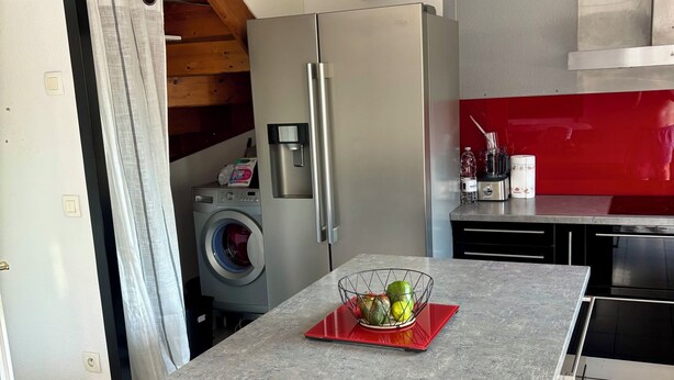 Une cuisine moderne dotée d’un îlot central, d’appareils électrom énagers en acier inoxydable et d’un pare-feu rouge.