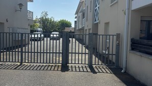 Une entrée fermée par un portail mène à un immeuble, avec un ciel dégagé au-dessus.