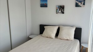 Une chambre à coucher comprenant un lit, une table de chevet, une lampe fixée au mur et deux tableaux encadrés.