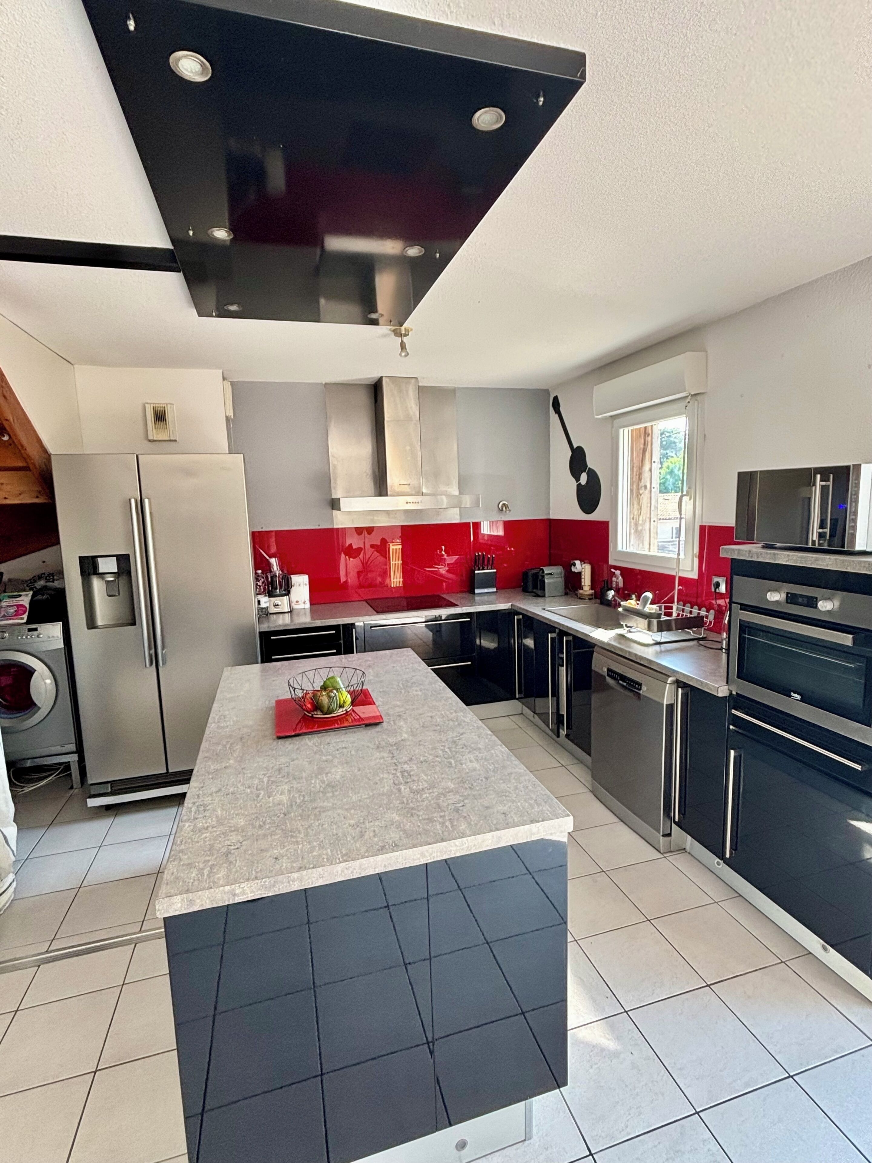 Een moderne keuken met roestvrijstalen apparatuur, een centraal eiland en een rode backsplash.