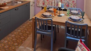 Ett kompakt kök med en matplats, med ett fönster dekorerat med blommiga gardiner, en inbyggd luftkonditionering och en kakelbeklädd vägg bakom diskbänken.