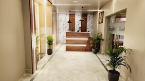 Un hall d’accueil d’hôtel avec un sol en marbre, un comptoir d’accueil en bois, des plantes en pot et un luminaire moderne.