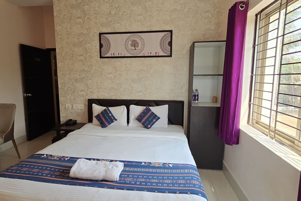 Habitació d'hotel ben ordenada amb llit, escriptori, cadira, armari i finestra amb cortines.