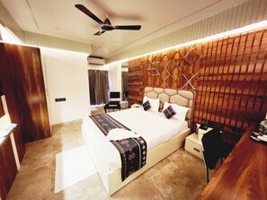 Una habitación de hotel moderna con una cama grande, un ventilador de techo, un cabecero de madera y una mesita de noche.