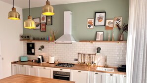 Una cocina moderna con armarios blancos, encimera de madera, lámparas colgantes y diversos utensilios de cocina.