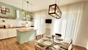 Una cocina moderna con una isla central, mesa de comedor con sillas y un televisor montado en la pared.