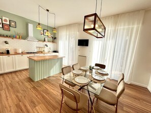A modern kitchen with a central island, dining table with chairs, and a TV mounted on the wall. - Spacious apartment in the heart of Umbria, for families and trips with friends. (Torgiano)