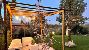 Un área de estar al aire libre techada, con una pérgola, luces colgantes y una pequeña mesa con una planta.