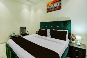 Ein Hotelzimmer mit Bett, Nachttisch, Sessel, einem Bild an der Wand und einer Lampe.
