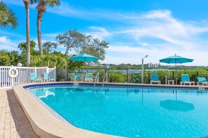 A swimming pool with blue water, surrounded by white fences and green chairs.