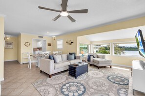 A spacious living room with a ceiling fan, a dining area, and a view of a lake.