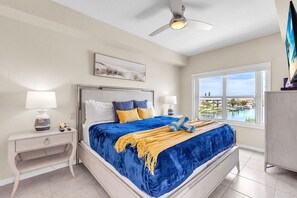 A bedroom with a bed, nightstands, a ceiling fan, a window with a view, and a painting on the wall.
