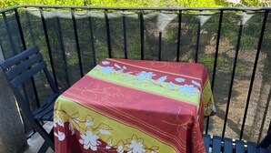 A balcony with a table covered by a floral tablecloth, two black chairs, and a view of greenery. - Gîte Studio Omu di Cagna (Monacia-d'Aullène)