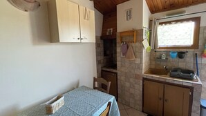 A compact kitchen with a dining table, wooden cabinets, a window, and a tiled backsplash. - Gîte Studio Omu di Cagna (Monacia-d'Aullène)