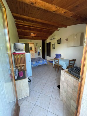 A compact kitchen with a stove, a sink, and a dining area with a table and chairs. - Gîte Studio Omu di Cagna (Monacia-d'Aullène)