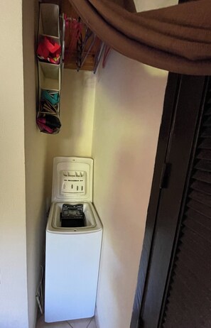 A compact room with a white electrical outlet, a small storage unit with various items, and a door with a window. - Gîte Studio Omu di Cagna (Monacia-d'Aullène)