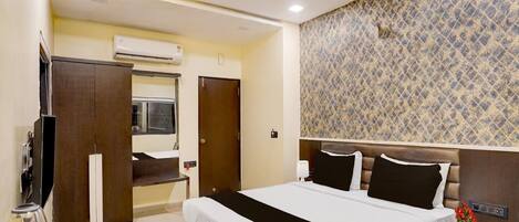 Une chambre d’hôtel avec un lit, un bureau et une chaise, une télévision, un ventilateur de plafond et un mur décoré de motifs.