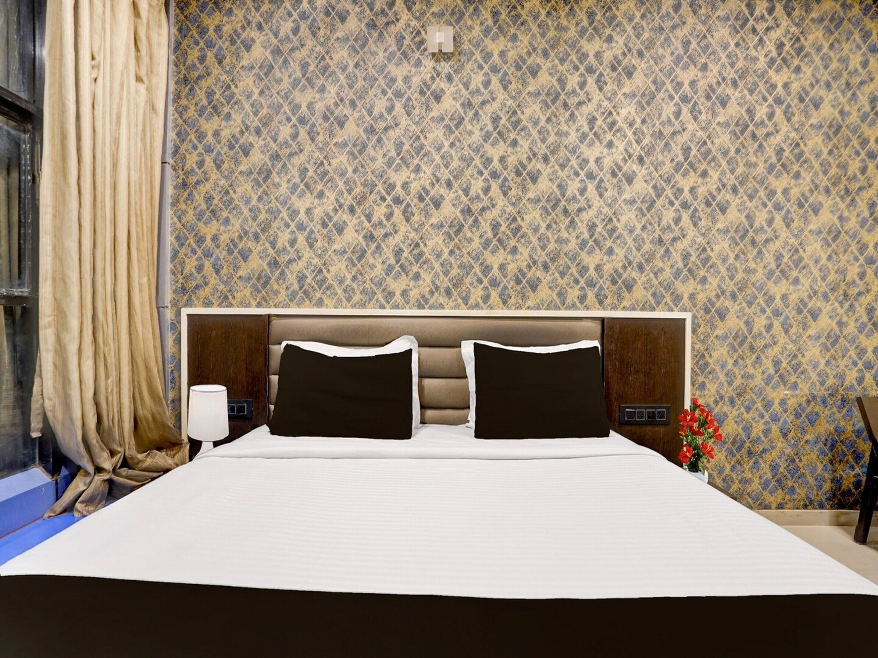 A hotel room with a large bed, a headboard, a nightstand, a lamp, and a window with curtains.