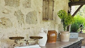 Eine Steinsäule, ein Holzbalken, eine weiße Vase, ein brauner Topf, eine Topfpflanze, eine Waage und ein schwarzes Schrank mit Schubladen.