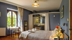 A bedroom with a large bed, a desk with a chair, a window with curtains, and a vase with flowers on the bedside table. - Suite room with private shower and separate toilet (Auch)