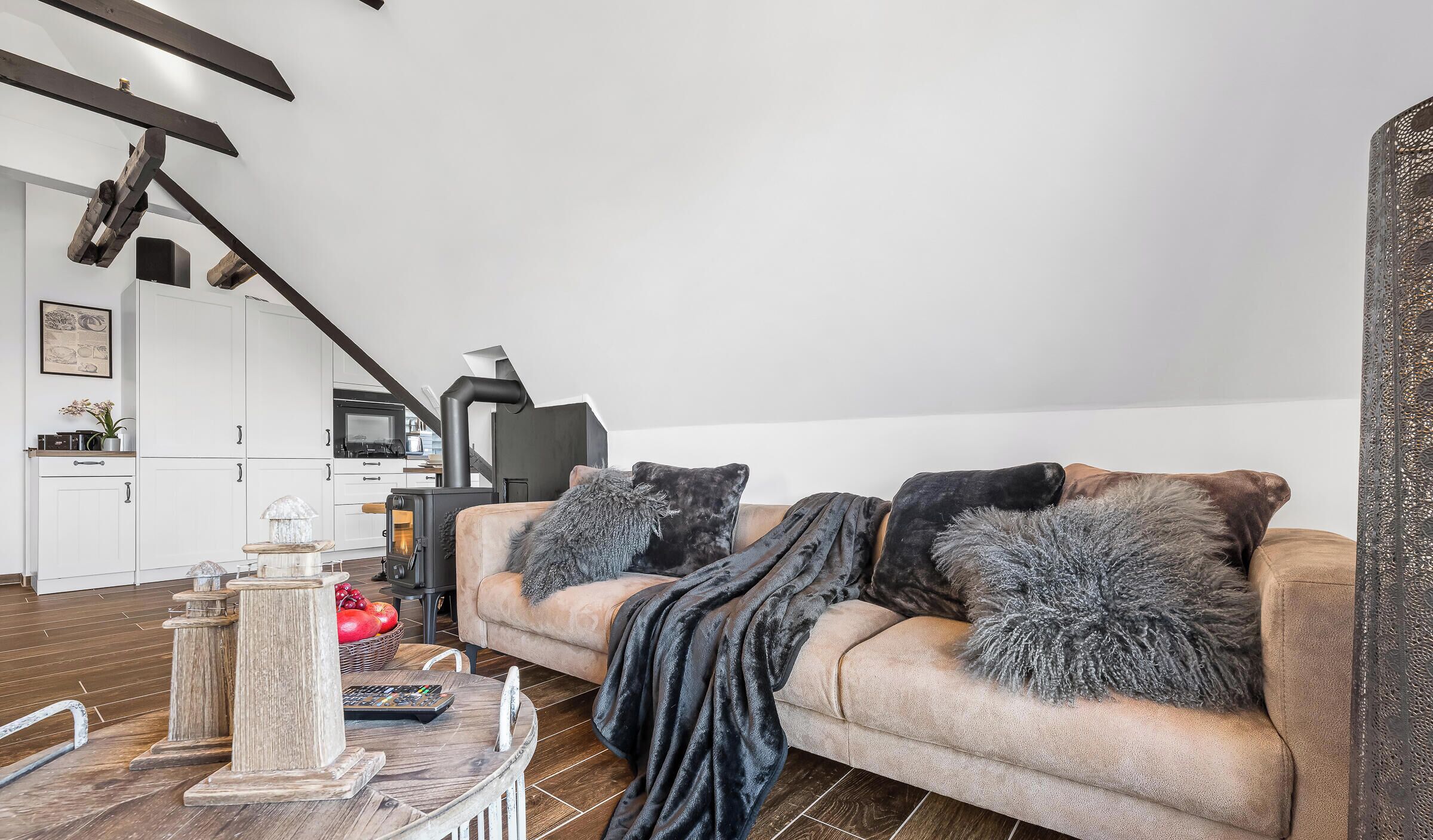 Un salon avec un canapé, une cheminée, une cuisine à l’arrière-plan et un escalier.