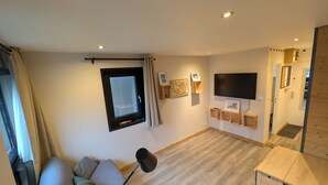 Ein modernes Wohnzimmer mit einer Couch, einem Fernseher, Holzregalen und einem Fenster mit Vorhängen.