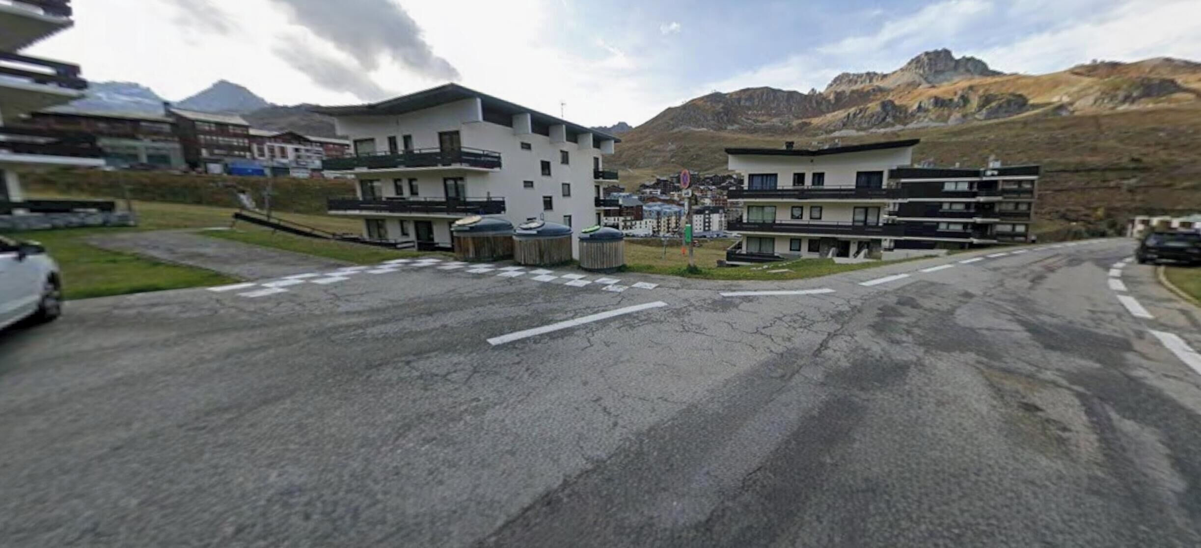 En väg leder fram till ett modernt byggnadskomplex med flera våningar och balkonger, omgivet av berg.